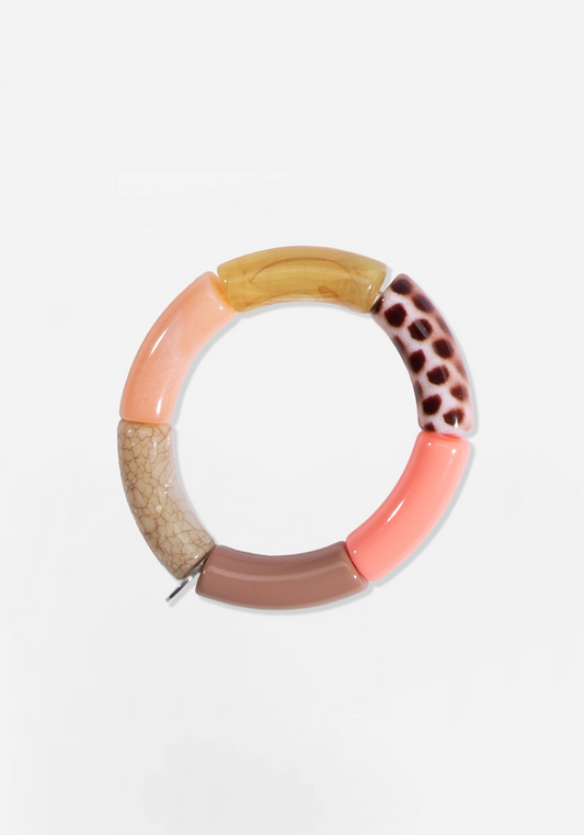 Elastiskt armband av böjda rörpärlor i varma, dova toner: persika, korall, gråbrunt och marmorerat bärnstensgult, samt en beige pärla med krackelerat mönster och en vit pärla med mörkbruna prickar. En liten silverfärgad bricka sitter mellan två av pärlorna.
