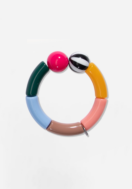 Elastiskt armband av böjda rörpärlor i mörkgrönt, ljusblått, gråbrunt, laxrosa och senapsgult. Upptill sitter två runda pärlor, en i cerise och en randig i svart och vitt. En liten silverfärgad bricka sitter mellan två av pärlorna.