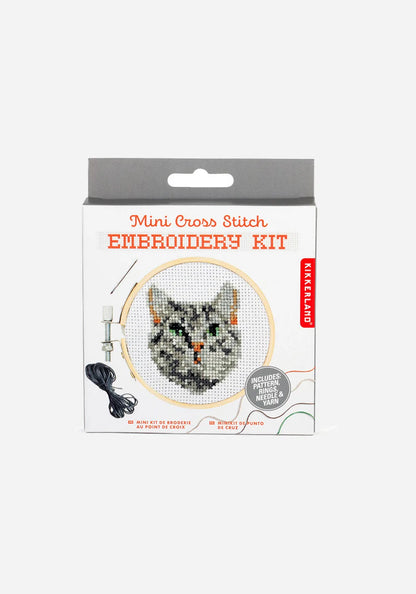Förpackning till ett broderikit i korsstygn med en broderad grårandig katt i en broderiram i bambu, med nål och grått garn.