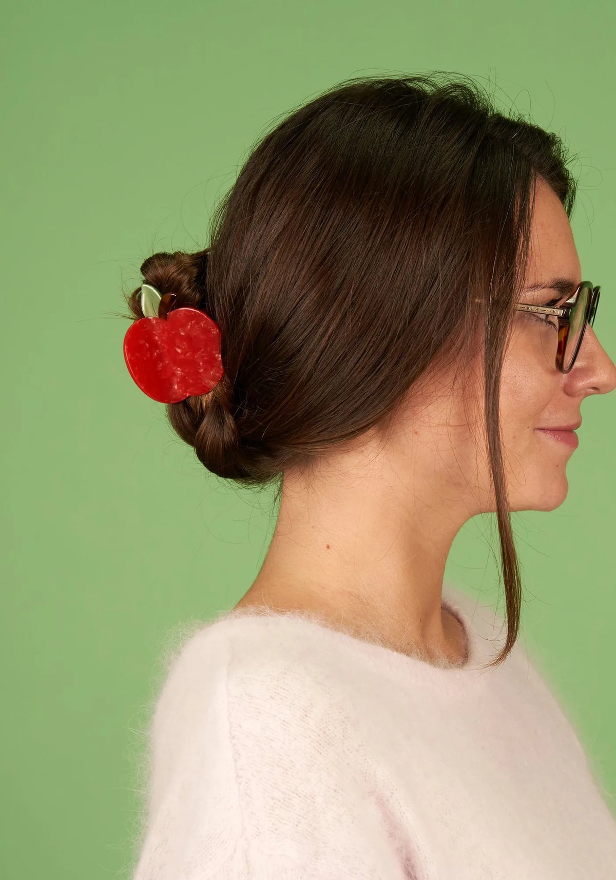 Kvinna i profil med lågt uppsatt knut som hålls av en röd äppelformad hårklämma från Coucou Suzette