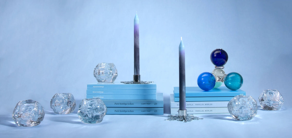 Juldukning i blått och silver: räfflade kronljus i toning från ljusblått till grått i silverfärgade ljusstakar formade som snöflingor, ljuslyktor Snowball från Kosta Boda i klart glas, en ljusstake av glaskulor i blått och turkos och böcker i ljusblått.