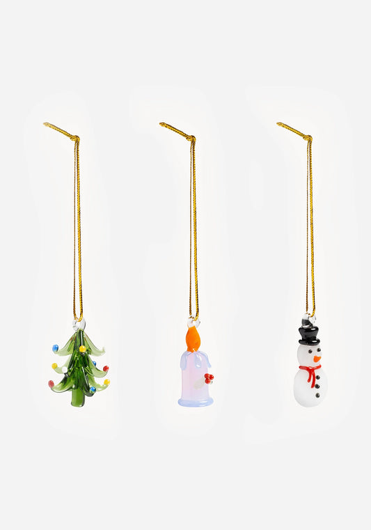 Tre julgranshängen i glas i guldfärgade snören: en grön gran med färgglada prickar, ett ljus med orange låga och en vit snögubbe med svart hatt och röd halsduk.