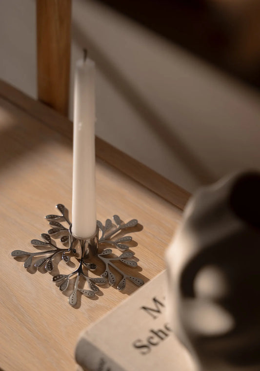 Ljusstake i stål med vitt kronljus på trähylla.