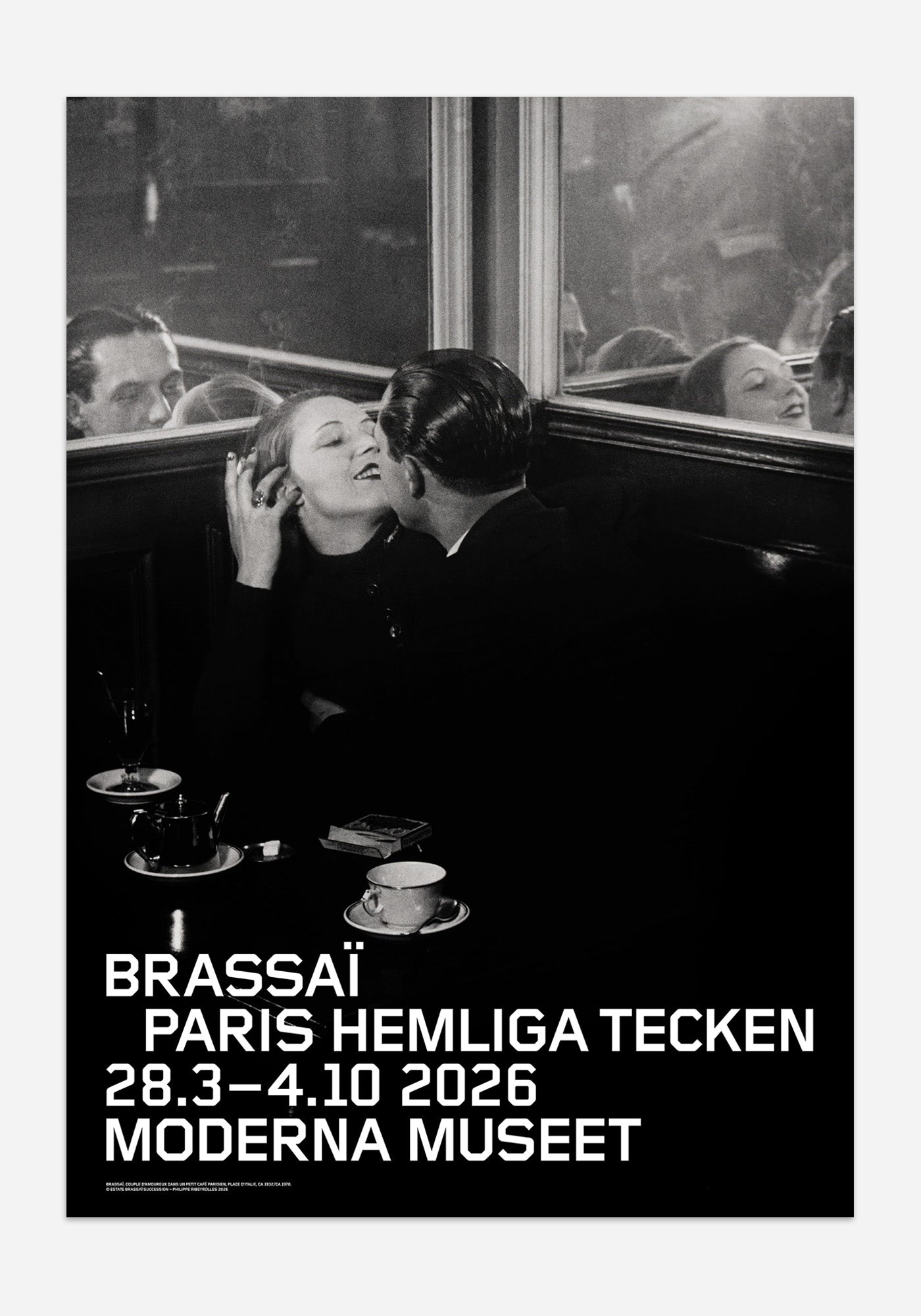 Svartvit utställningsaffisch från Moderna Museet för Brassaï-utställningen Paris hemliga tecken. Motivet visar ett stämningsfullt fotografi av ett kyssande par i en cafésoffa, med tekoppar på bordet och speglande glas i bakgrunden.