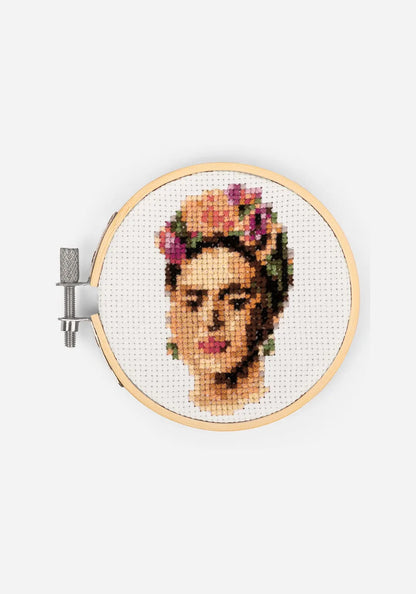 Färdigt korsstygnsbroderi i en broderiram i bambu, med ett porträtt av Frida Kahlo med blomsterkrans i håret.