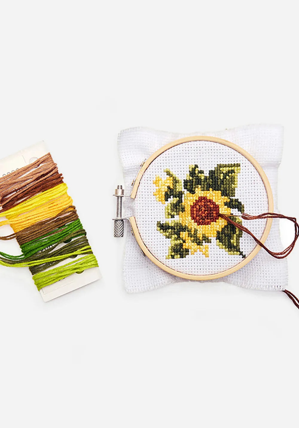 Broderiram i bambu med en broderad gul solros på vitt tyg, bredvid ett kort med broderigarn i brunt, gult och grönt.